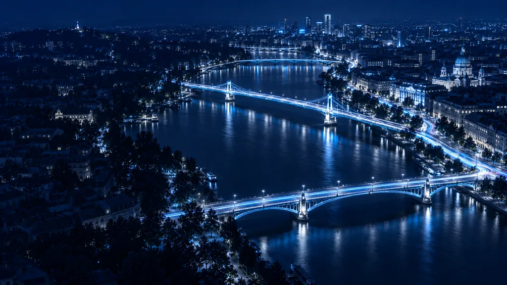 Aerial night view of two city districts joined by cyan-lit bridges across a river